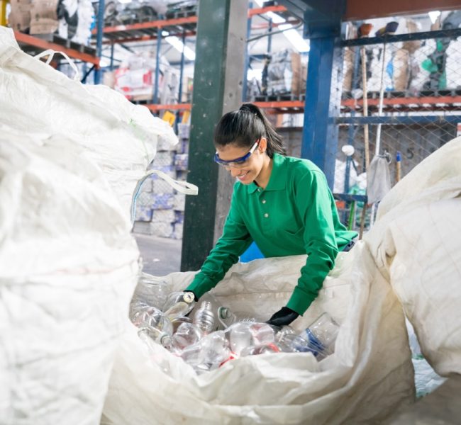 Woman working in a recycling factory sorting some bottles and looking very happy - environmental concepts